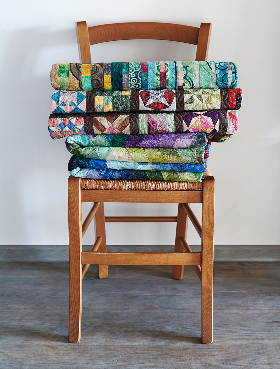 chair with a pile of brightly colored finished quilts folded
