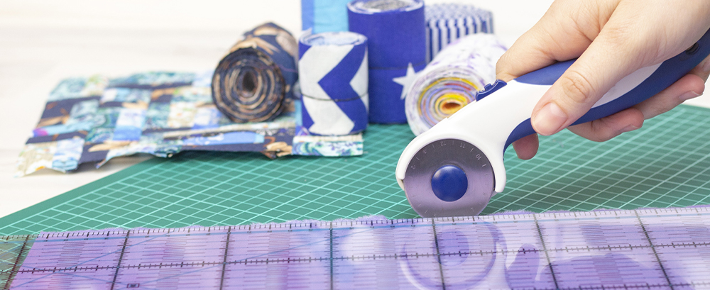 rolls of fabric and quilting piece in background cutter in foreground